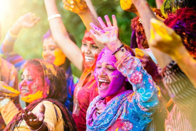 Women celebrating the Holi festival in India with vibrant colored powder in the air and on themselves on women's trip to India.