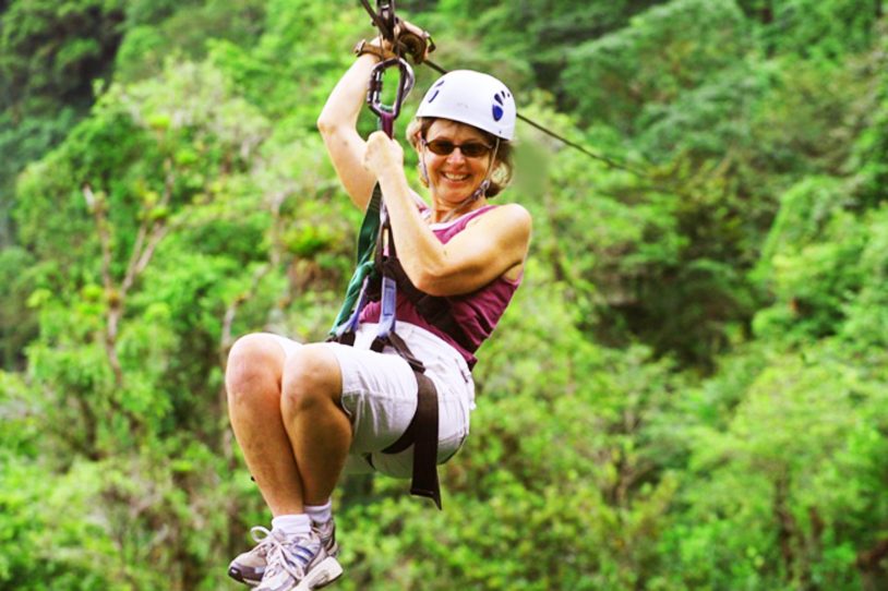Close up of woman ziplining and smiling across trees.