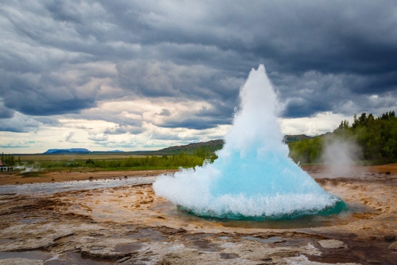 Famous Strokkur fountain geyser hot blue water eruption with cloud sky and surrounding Icelandic landscape, Iceland