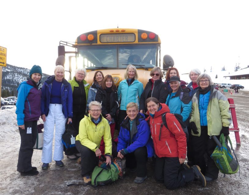 Group of women geared up for skiing taking a group photo in front of a bus