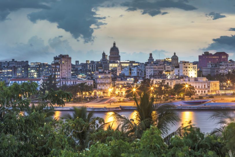 Illuminated Havana city against sky. Capitolio amidst cityscape at dusk. Buildings and trees are by sea.