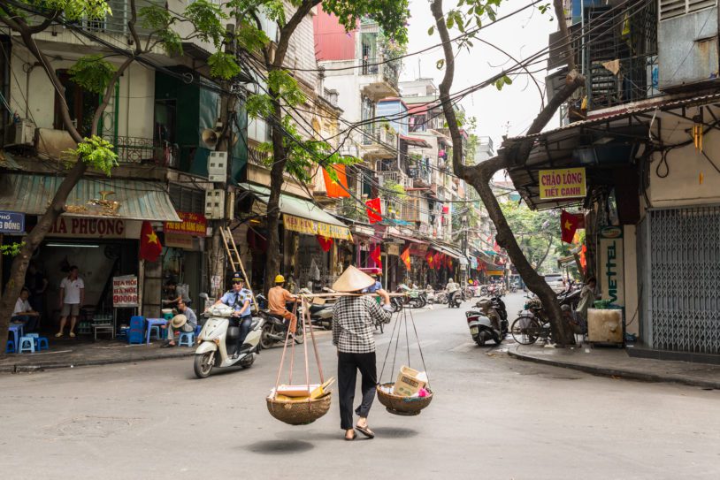 Street vendor transporting goods in baskets balanced across shouldersin Hanoi