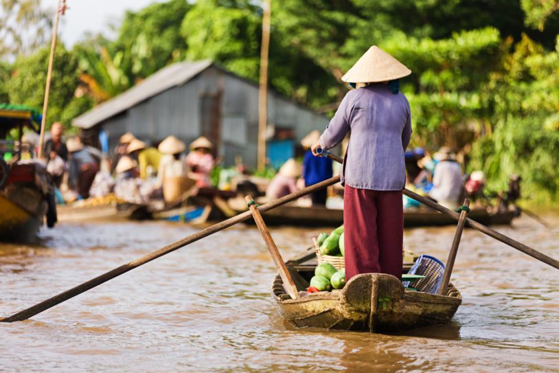 Vietnamese fruits seller - woman rowing boat in the Mekong river delta selling fruits, Vietnam.