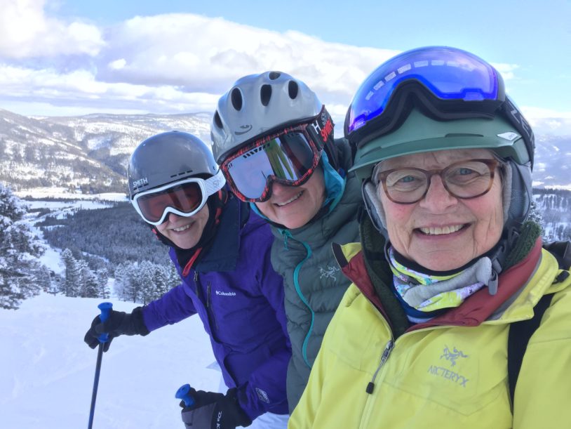 Three women with ski helmets and goggles at the top of a ski slope