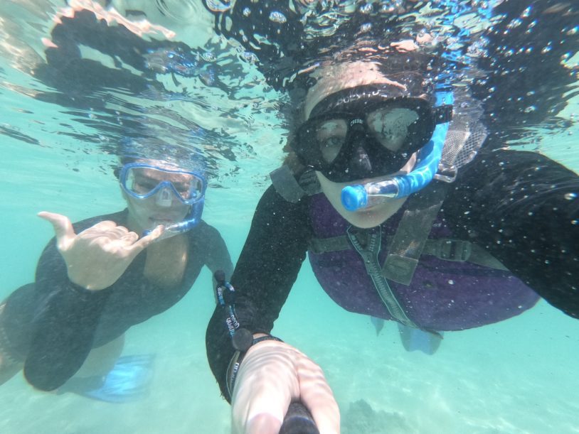 Two women snorkeling with masks under water and looking into the camera