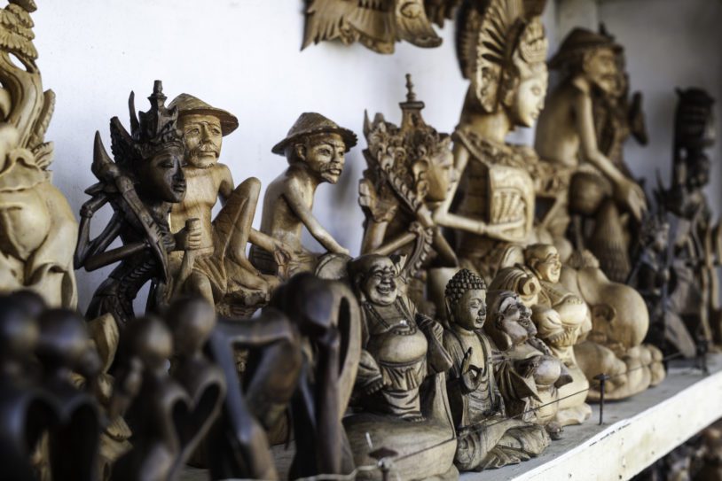 Wooden carvings of fishermen and Buddhas on the shelf of a beachside market. Some of the many crafts that can be found in Bali.