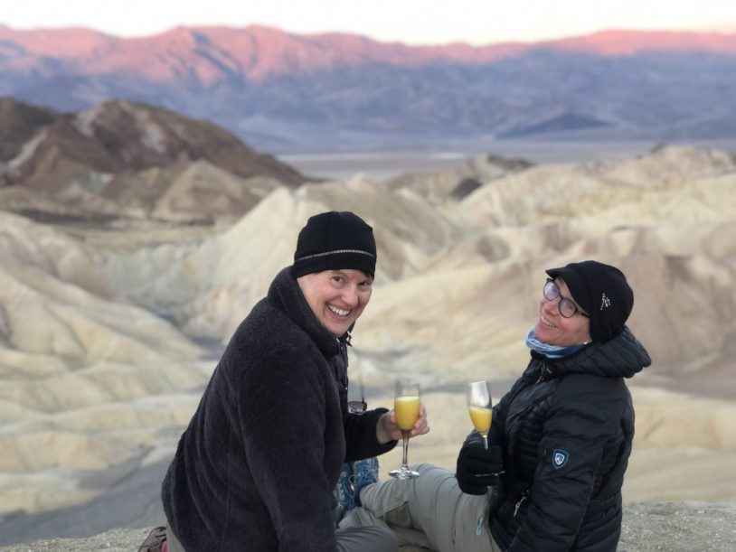 Two travelers toasting a drink at sunset over a Death Valley viewpoint