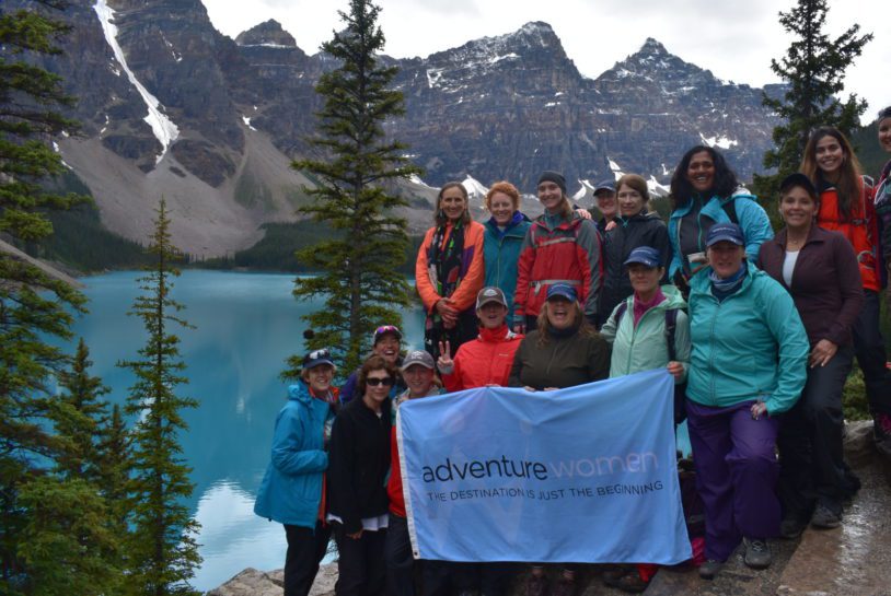 AdventureWomen group posing with their flag next to brilliant blue lake