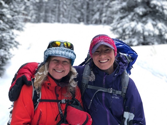 Two women smiling in red and purple winter jackets and gear