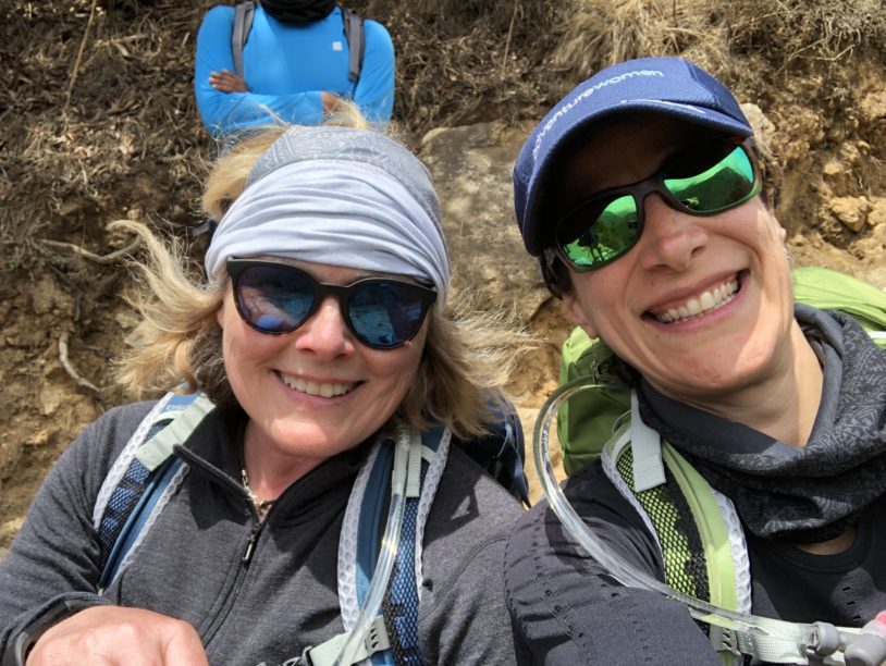 Two women with sunglasses and hiking gear smiling for the camera
