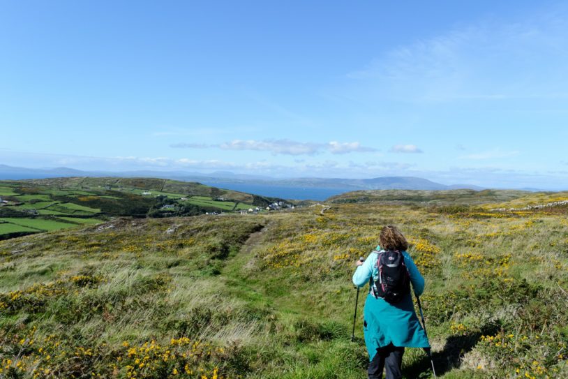 Hiker in blue walking into the breeze crossing Ireland